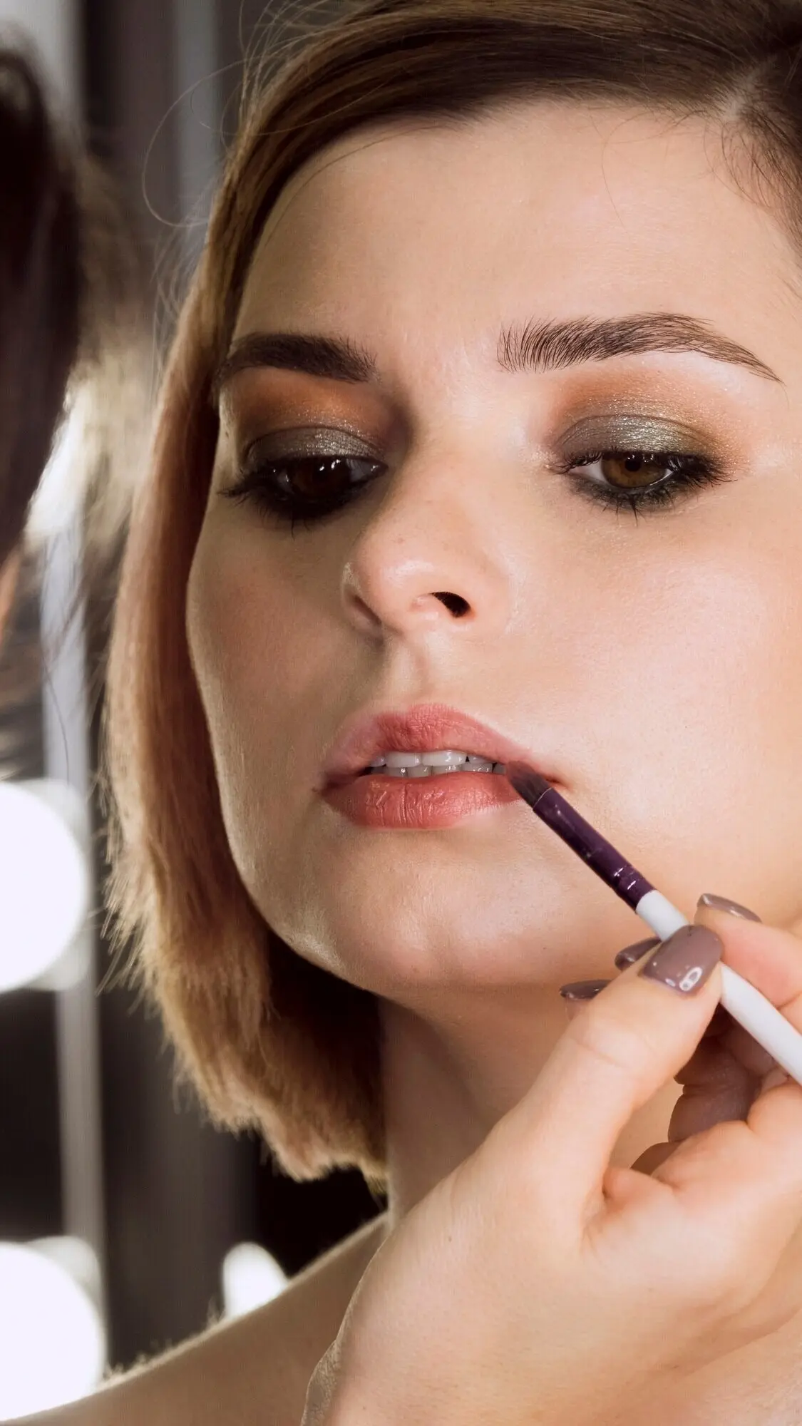 Eine Hand trägt einem Kunden Lippenstift auf.